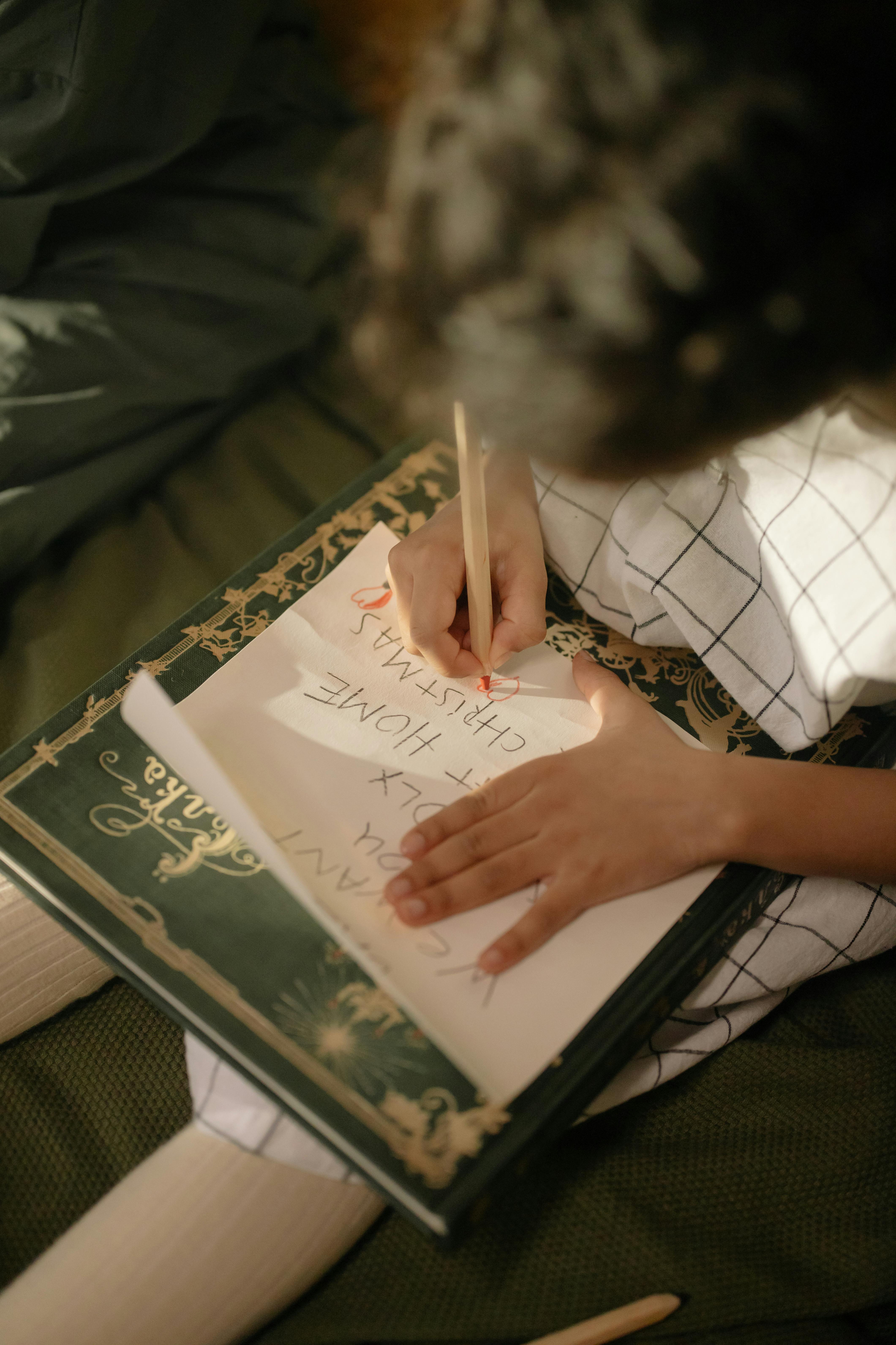 A child drawing on paper with colored pencils, composing a Christmas wish list.