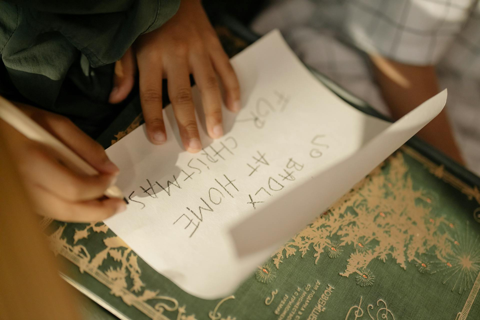 A child's hands writing a Christmas list on paper, emphasizing the joy of holiday preparations.
