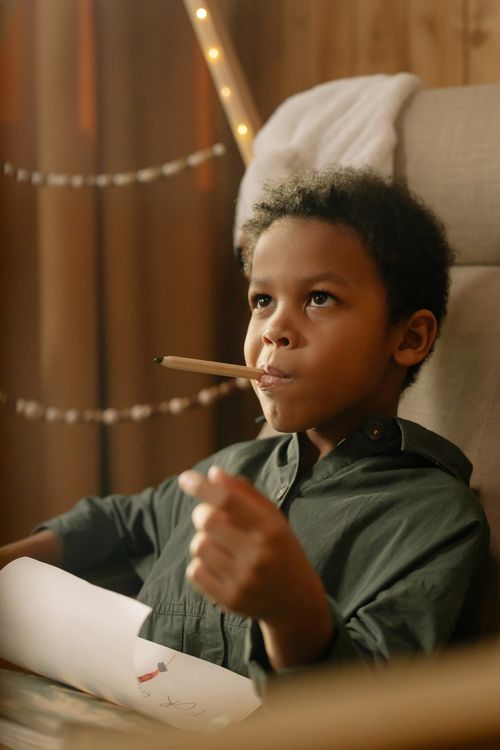 Free A thoughtful child holding a pencil while drawing indoors with warm lighting. Stock Photo