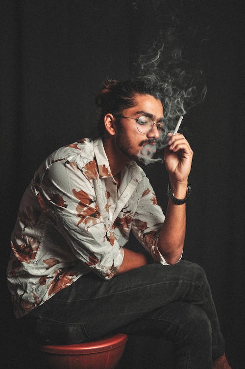 Man in Brown and White Floral Button Up Shirt Smoking Cigarette