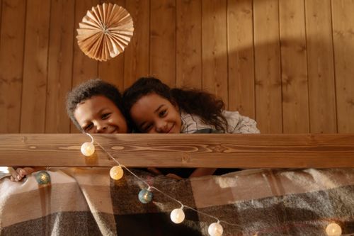 Free Two happy children cuddling on a cozy indoor bed with warm lighting. Stock Photo