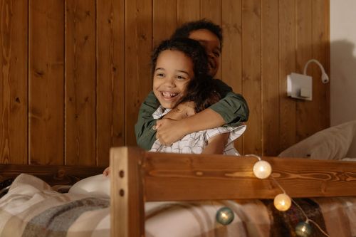 Free Two happy children share a warm hug on a cozy bed, surrounded by soft lighting. Stock Photo