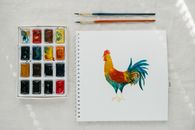 Picture of cock painted with watercolors placed on table
