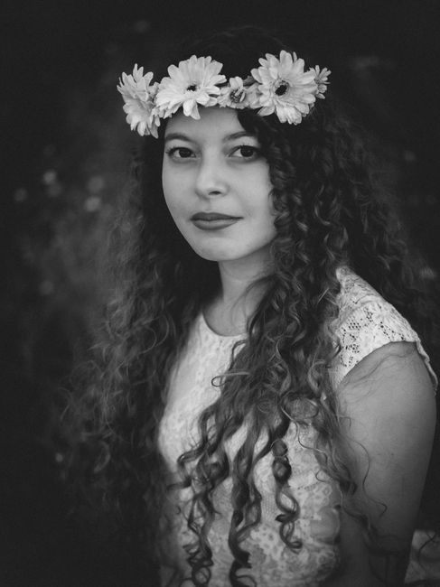 Young female in elegant dress with floral wreath on head and curly long hair looking at camera