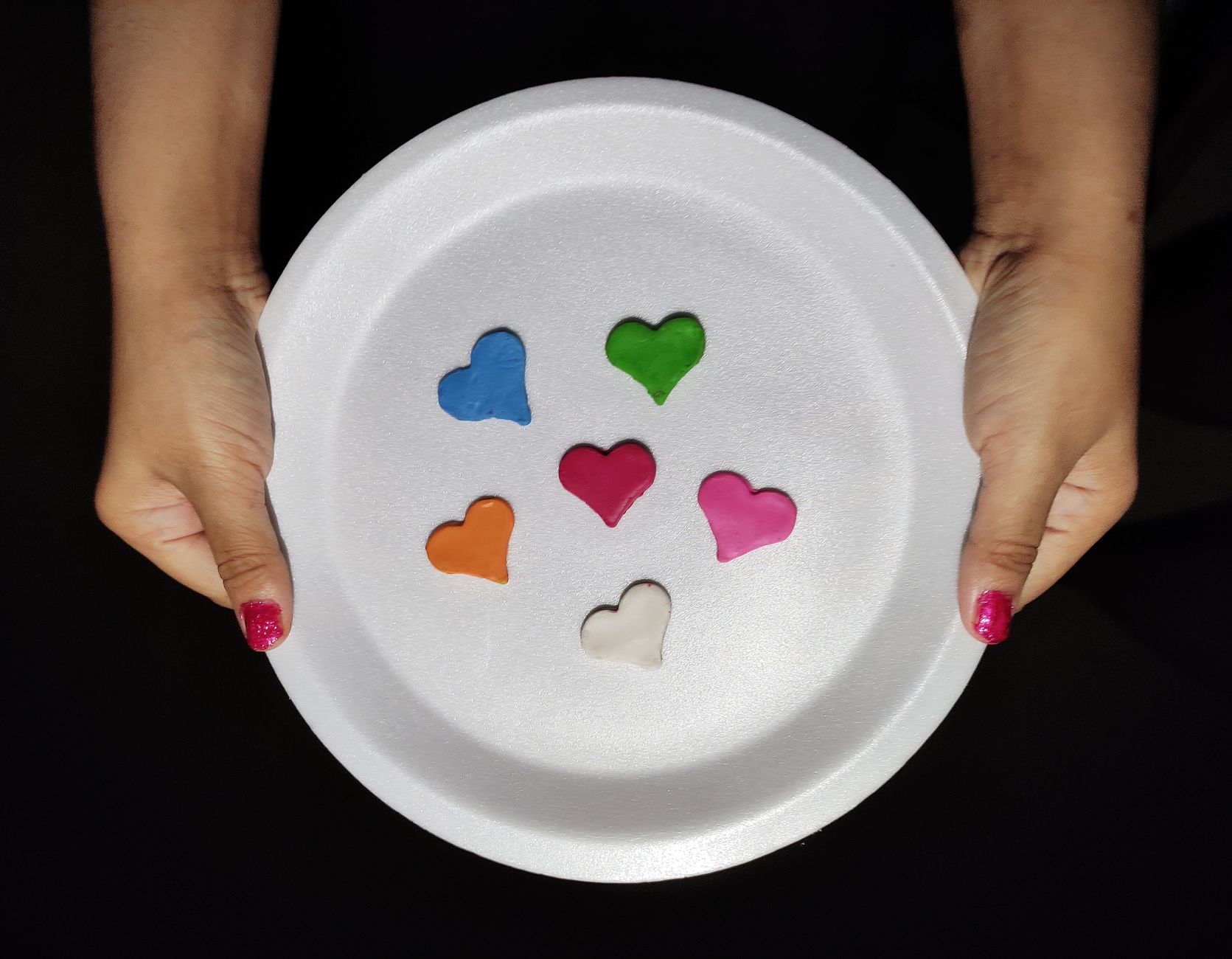 Multicolored heart shapes on a disposable plate held against a black background.