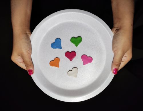 Free Multicolored heart shapes on a disposable plate held against a black background. Stock Photo