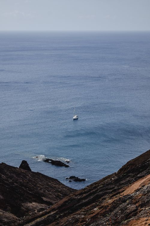Free Scenic view of a sailboat on the Atlantic Ocean near Madeira's rugged cliffs on a clear day. Stock Photo