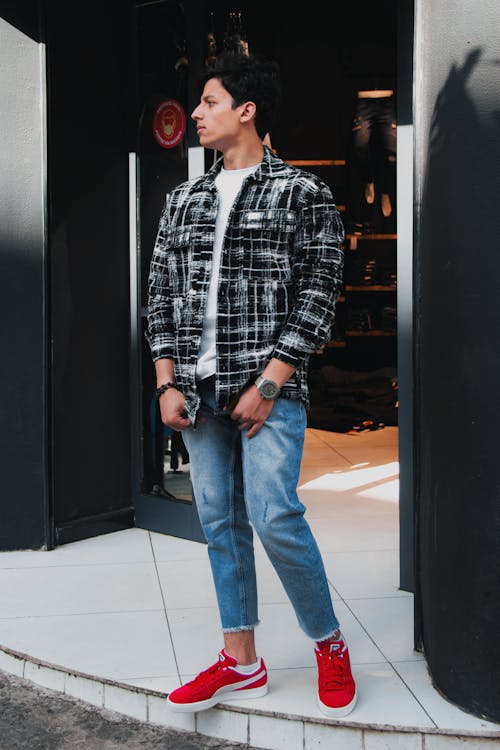 Man in Black and White Plaid Long Sleeves and Blue Denim Jeans Standing Beside Door 