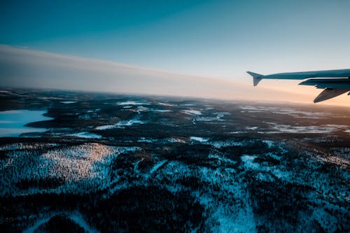 Plane flying over snowy terrain with trees and lake at sundown