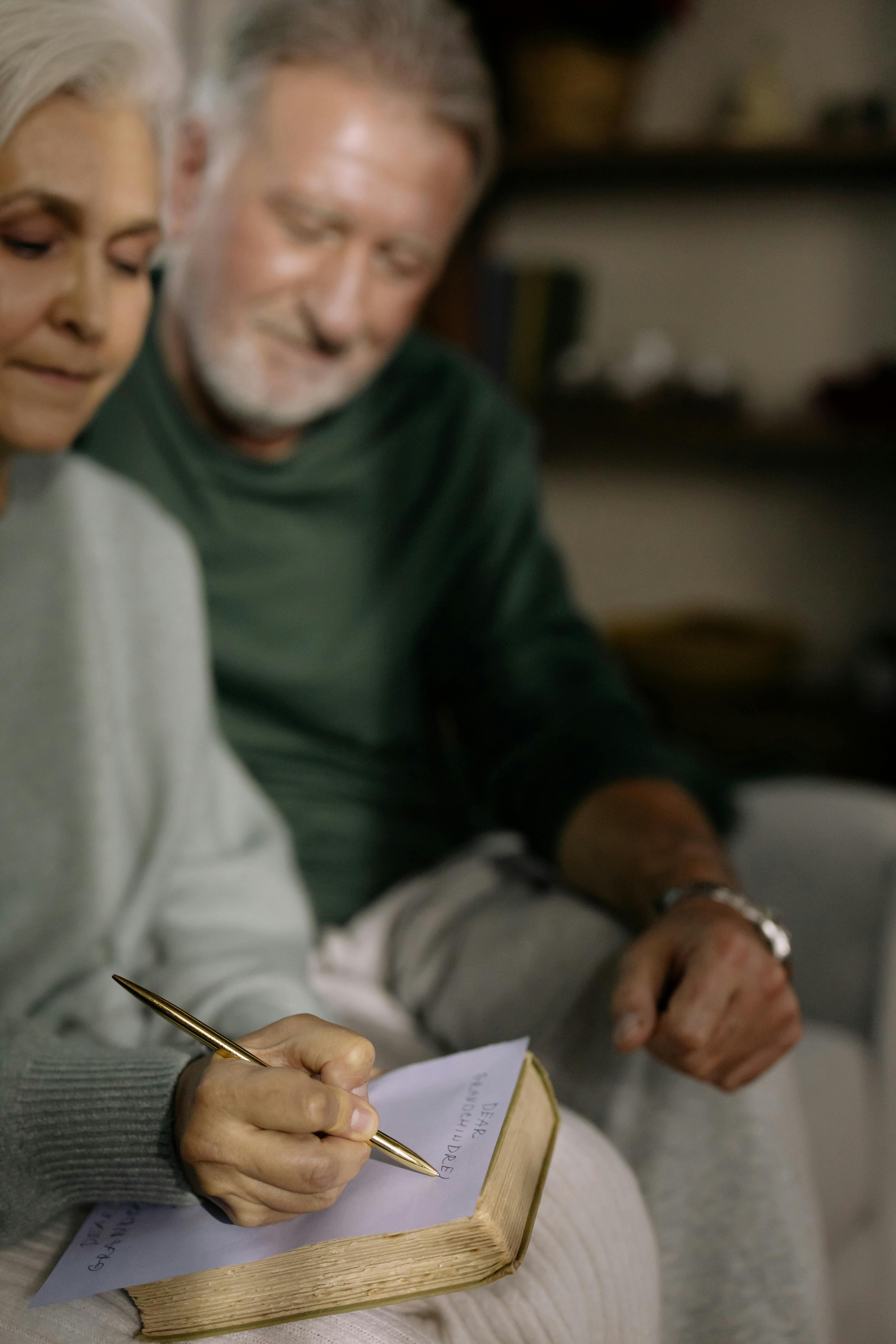 elderly woman sitting beside her husband writing on a paper