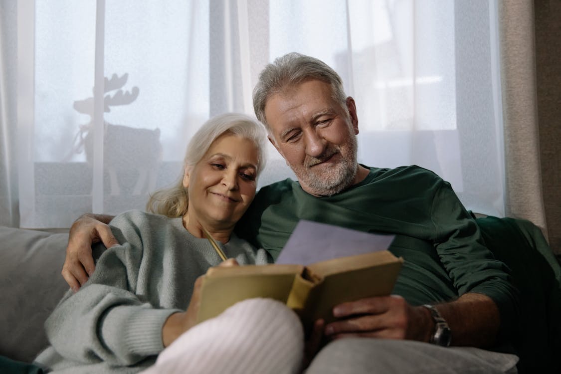 Free Man in Green Sweater Holding Book Beside Woman in White Sweater Stock Photo