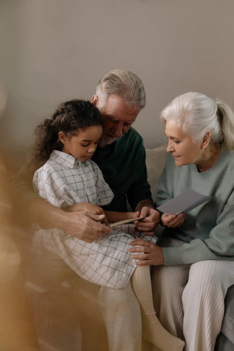 Grandparents And A Girl Sitting On A Couch While Reading A Greeting Card