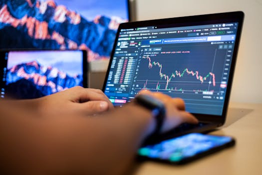 Hands typing on a laptop displaying financial trading charts, indicating active online trading work.