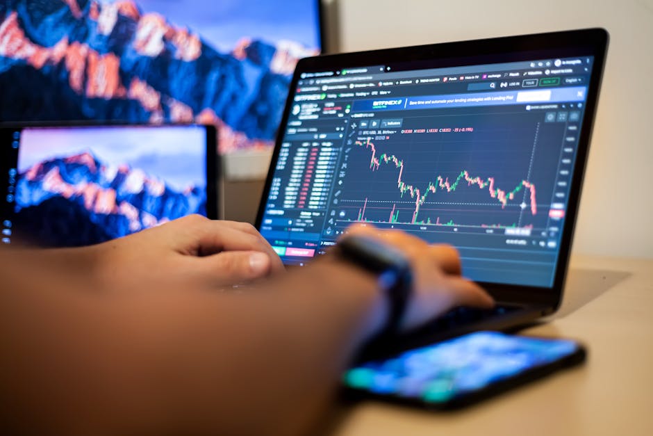 Does $100 Actually Help You Start Investing? Hands typing on a laptop displaying financial trading charts, indicating active online trading work.