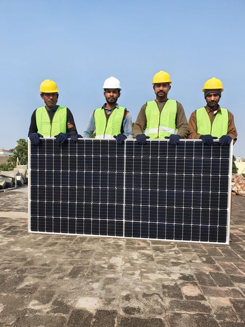 Free Group of construction workers holding a solar panel on a sunny day, wearing safety gear. Stock Photo