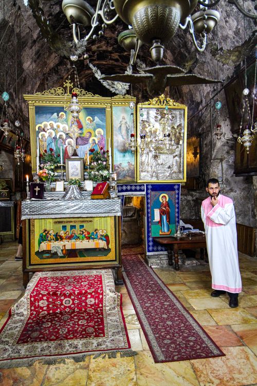 Free A priest stands beside an adorned altar inside a historic church in Israel, showcasing vibrant religious art. Stock Photo