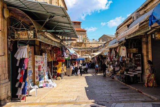 Bustling market alley in Jerusalem's Old City featuring shops and tourists under a sunny sky.