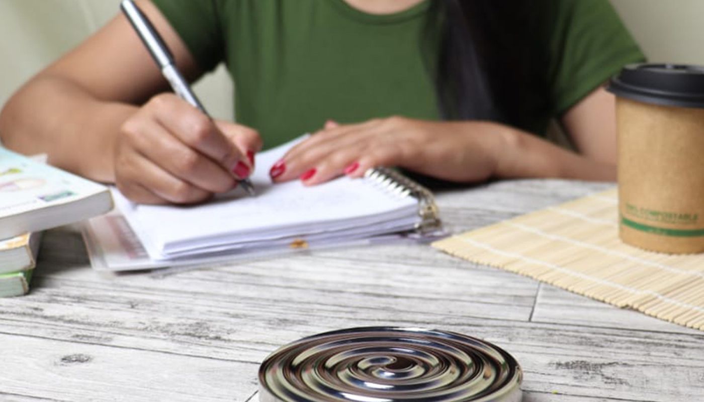 A person writing figures in a spiral notebook at an outdoor table