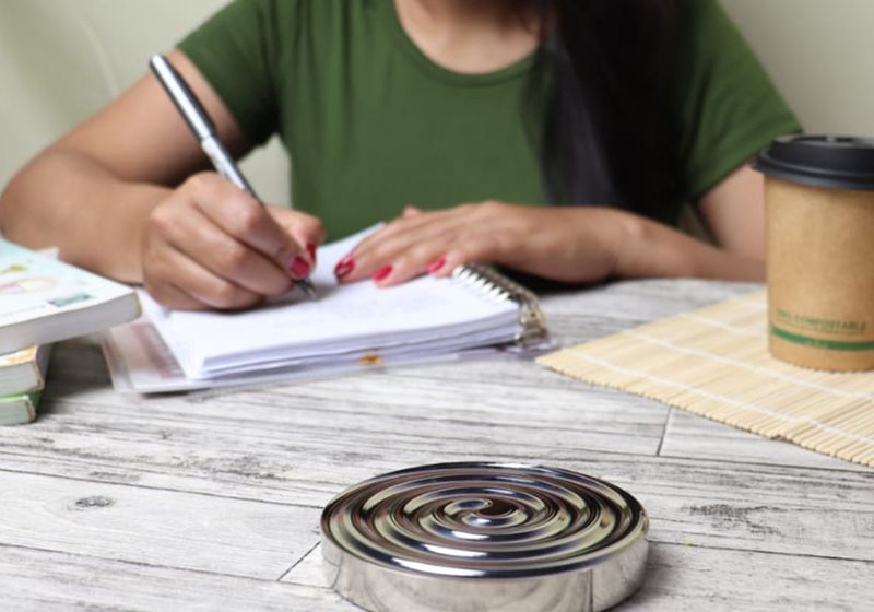 A person writing figures in a spiral notebook at an outdoor table