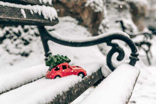 Free A miniature red car with a Christmas tree on a snowy bench captures the essence of a frosty winter holiday. Stock Photo