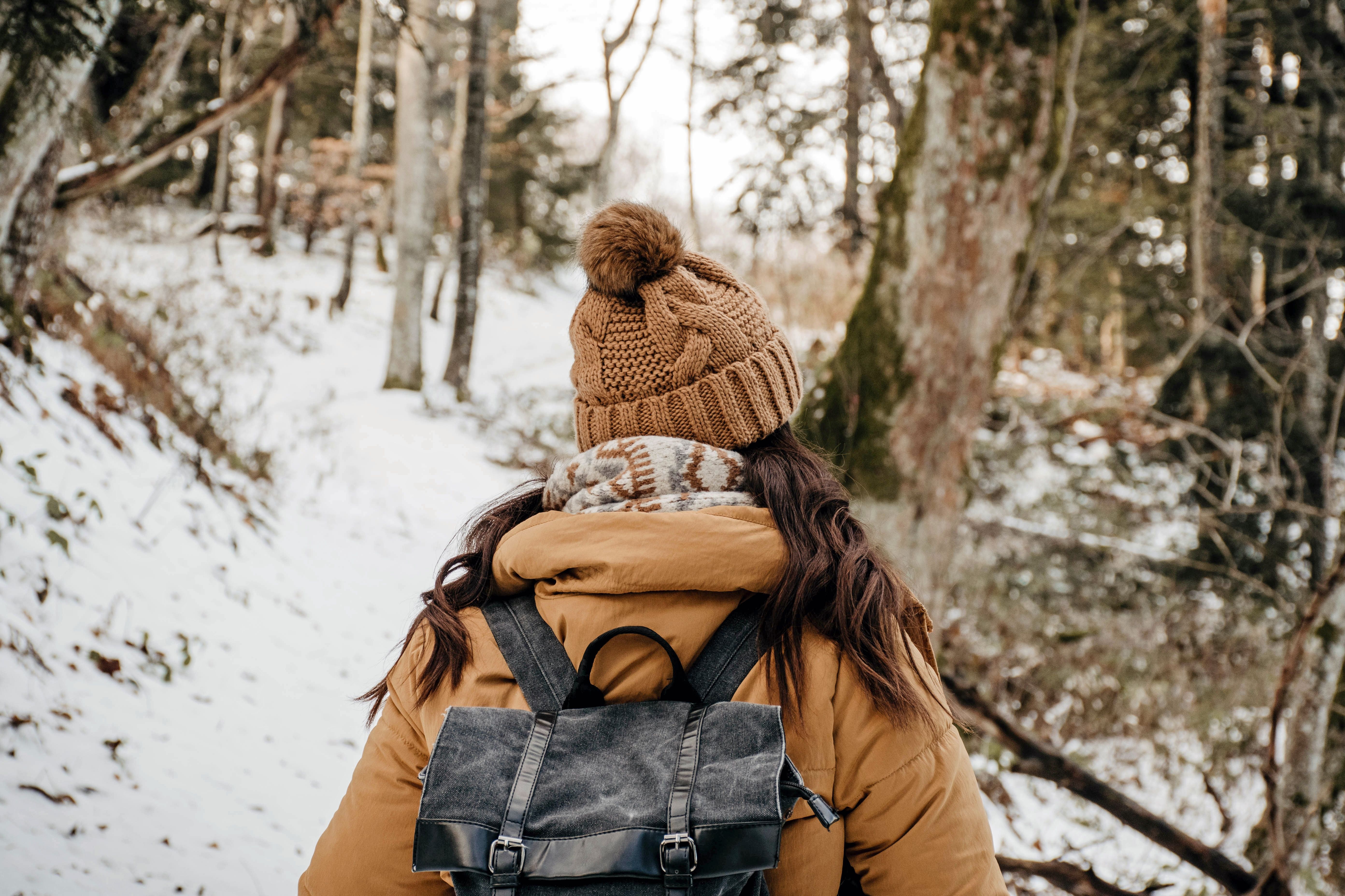 A woman in warm clothing exploring a snowy forest, showcasing winter adventure and hiking lifestyle.