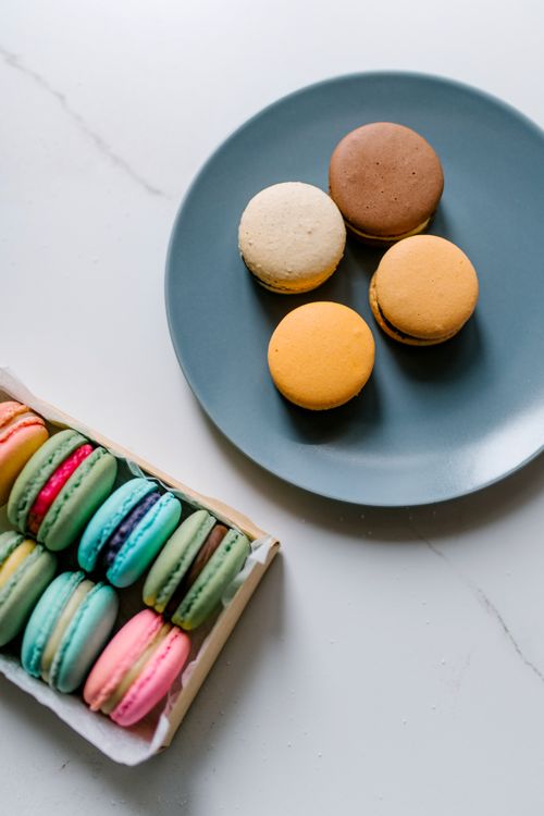 Free Vibrant French macarons arranged on a plate and in a box on a marble surface. Stock Photo