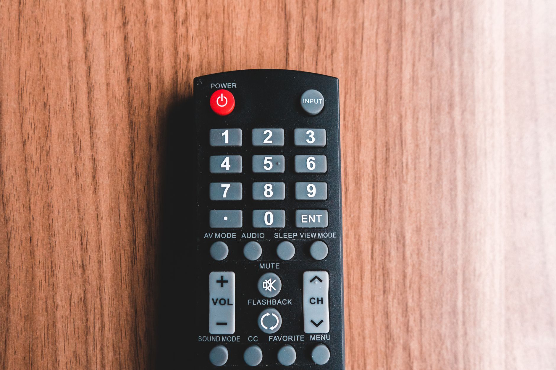 Top view of plastic remote control with rows of buttons representing power and mute symbols on brown background