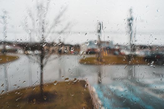 Glass wall with transparent aqua drips and fluids against urban street on rainy day in autumn