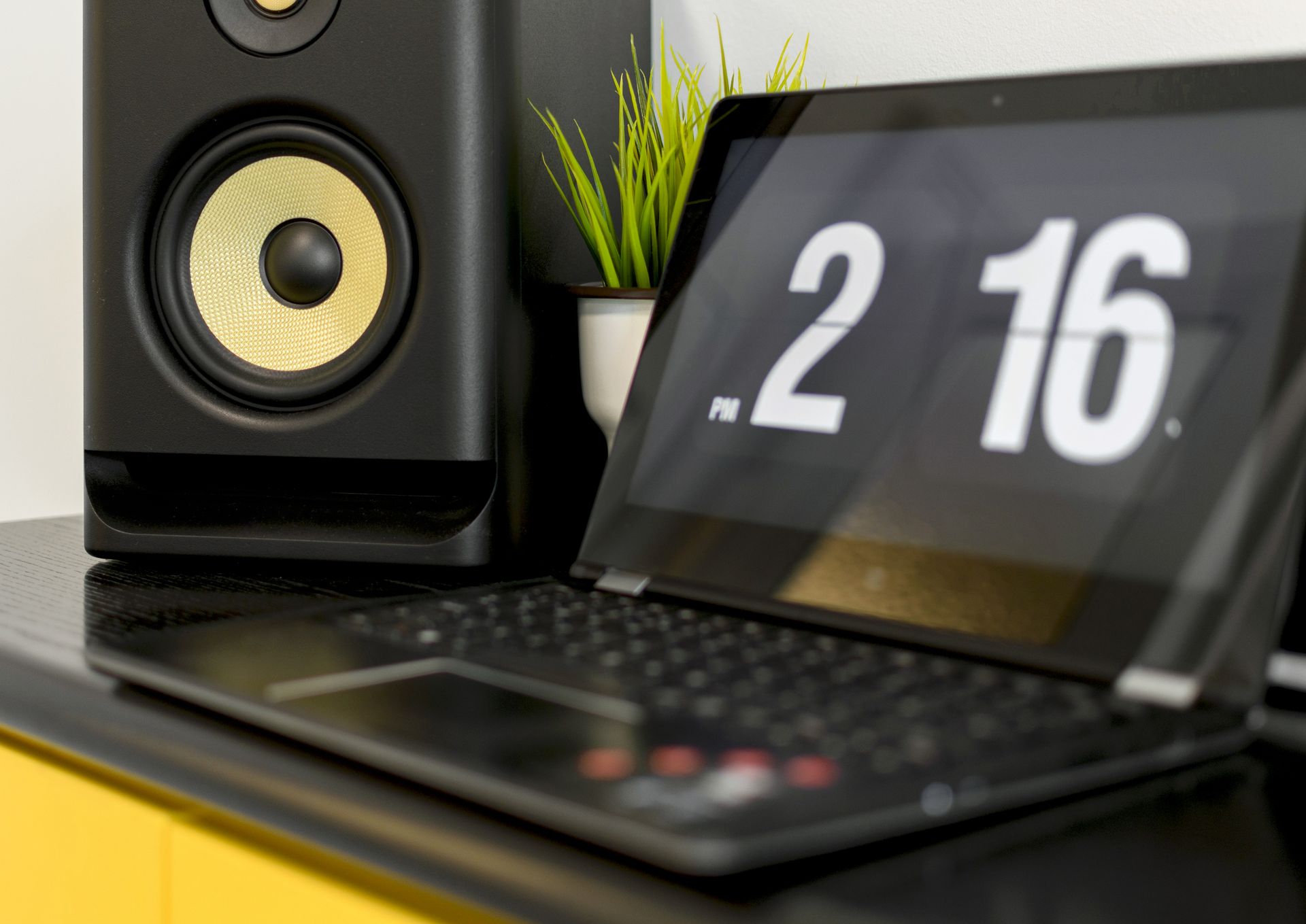 A sleek setup showing a laptop with a flip clock and a stylish speaker on a desk.