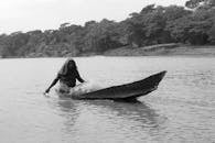 Woman in Black Dress Lying on Black and White Surfboard on Body of Water