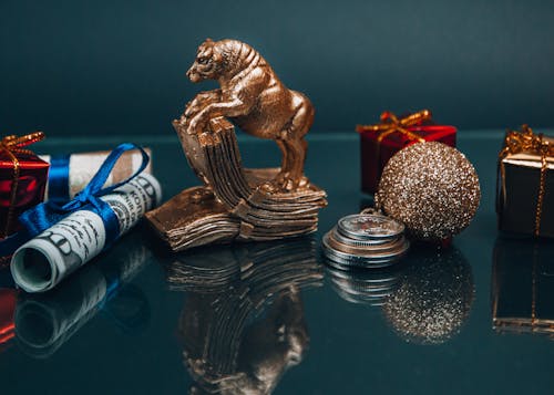 High angle composition of Ox year symbol figurine and wrapped presents placed on mirrored table with coins and rolled and tied dollar banknotes