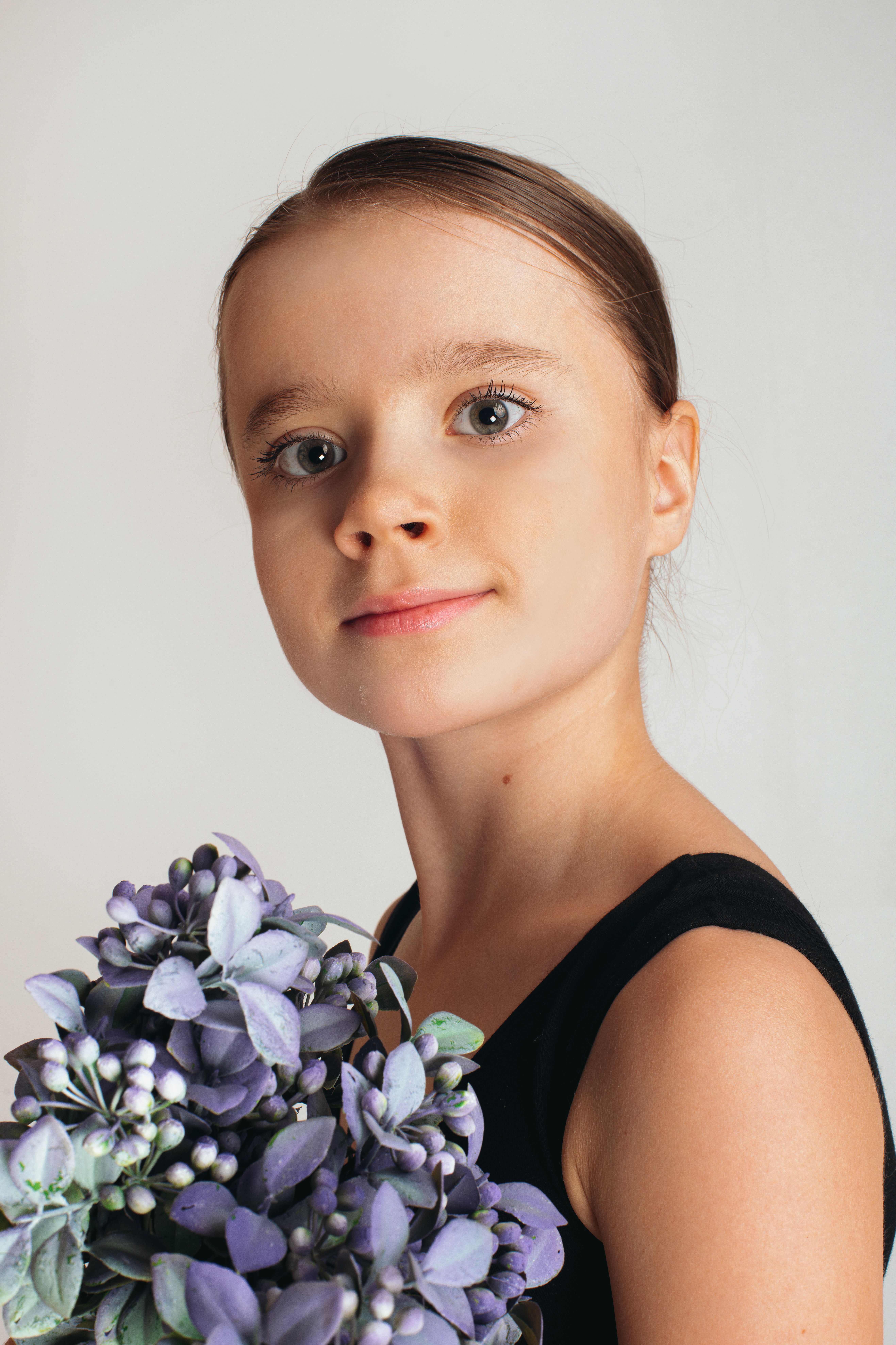 Contemplative girl in black dress with bunch of violet flowers looking at camera on white background