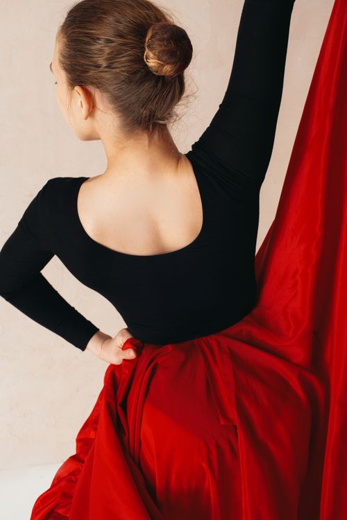 Free Back view of anonymous young female flamenco dancer in big red skirt with raised hand on cream background Stock Photo