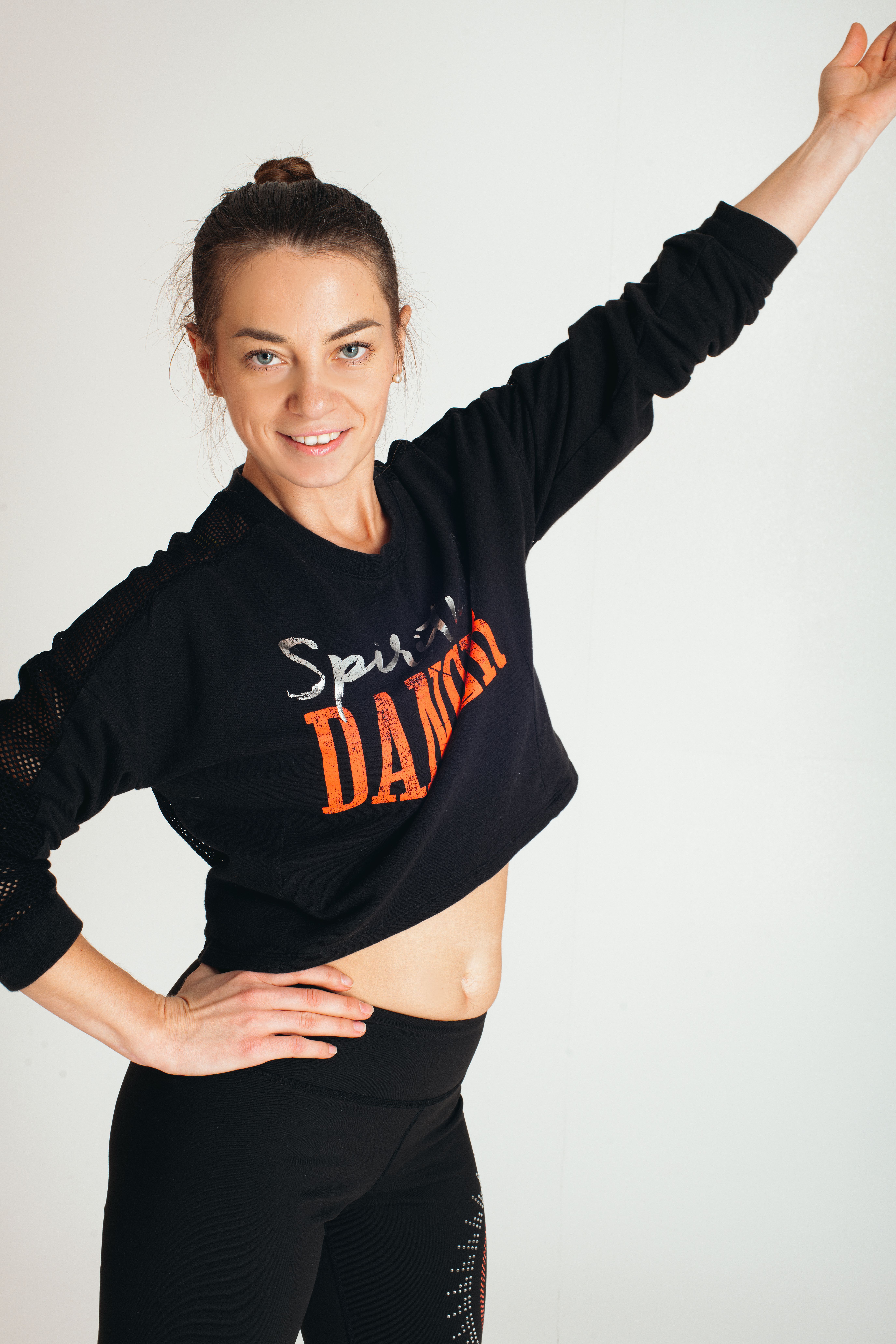 Smiling woman in sports attire posing confidently with one hand raised against a white background.