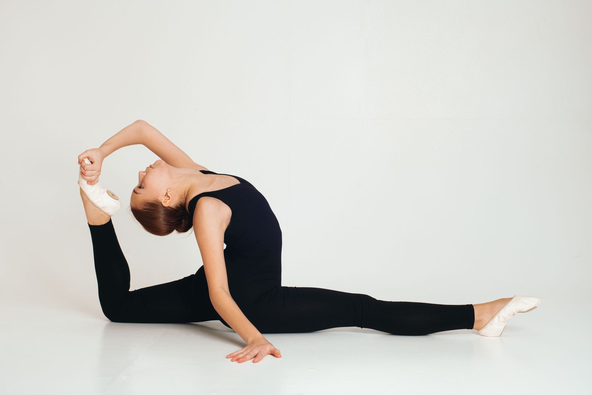 Elegant ballerina in black activewear demonstrates a perfect split in a studio setting.