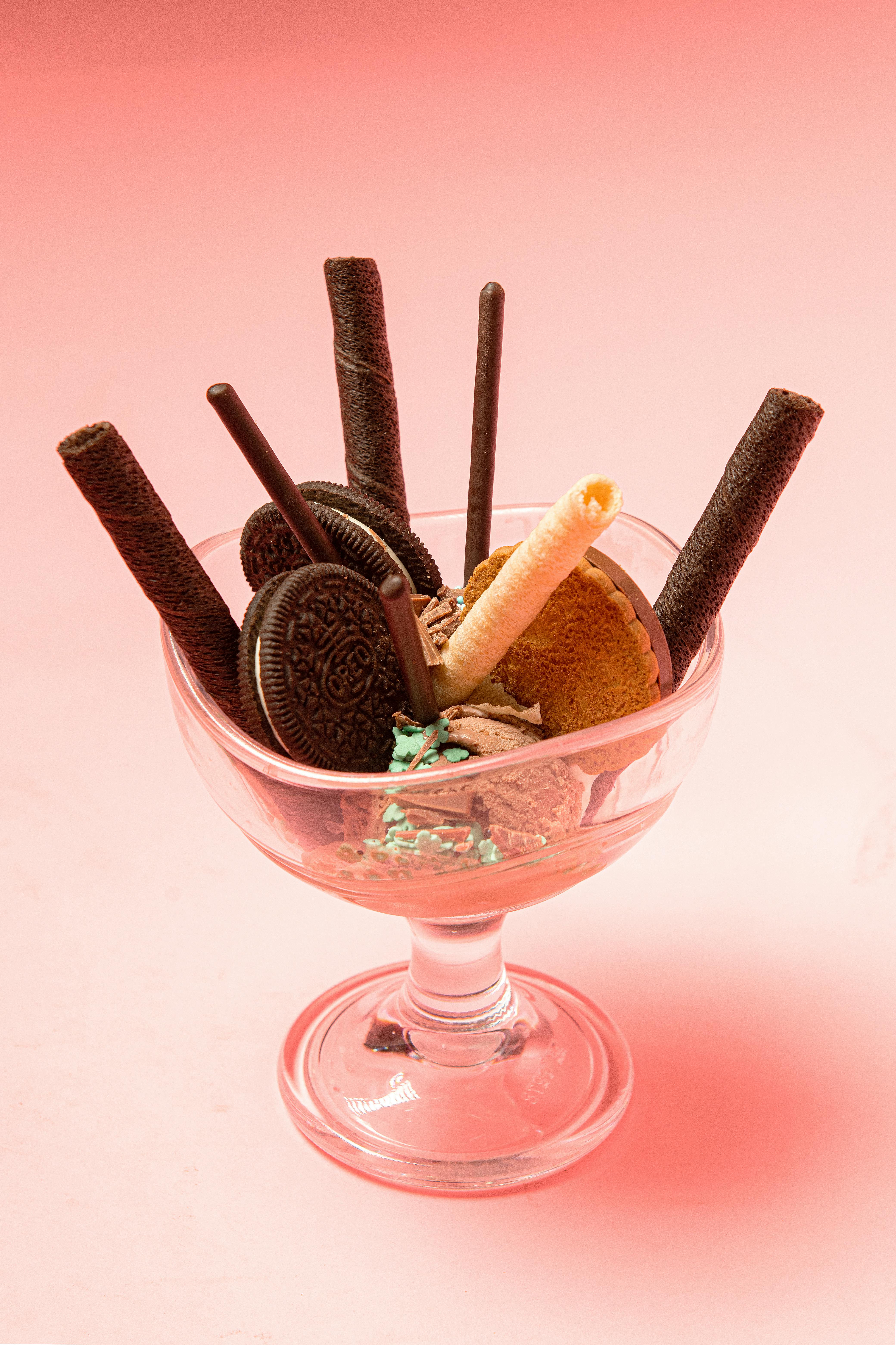 Glass of yummy ice cream with chocolate and vanilla waffle rolls near crunchy biscuits and sprinkles