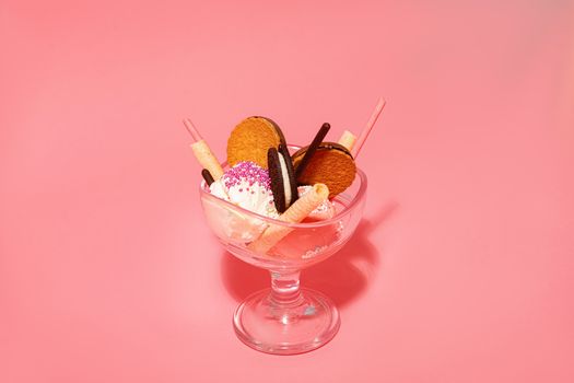 Glass of delicious gelato scoops with vanilla waffle rolls and crispy biscuits with smooth filling on pink background