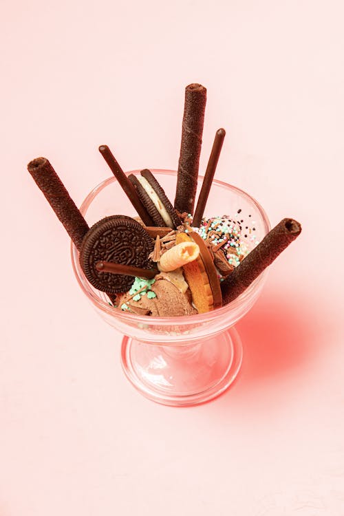 High angle of yummy gelato with chocolate and vanilla waffle rolls near biscuits and sprinkles in glass