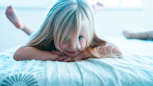 Free Adorable young girl with blonde hair smiling while lying on a bed. Stock Photo