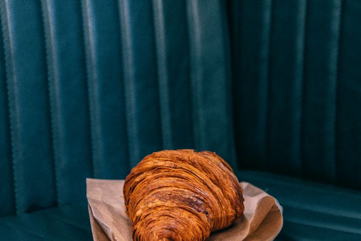 Tasty freshly baked croissant on parchment paper placed on dark leather sofa in daylight