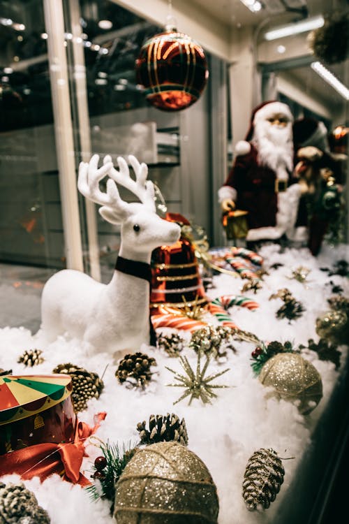 Store window with festive decorations including sparkling baubles deer and Santa figurines placed on fluffy artificial snow