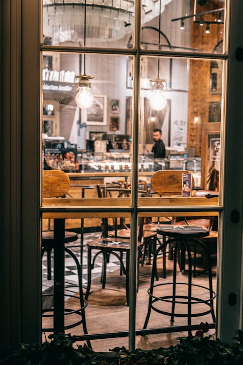 Through glass interior of cafe with wooden furniture and barista working at counter