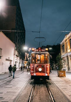 A vintage red tram travels through a lit street in Istanbul at night, capturing urban charm.