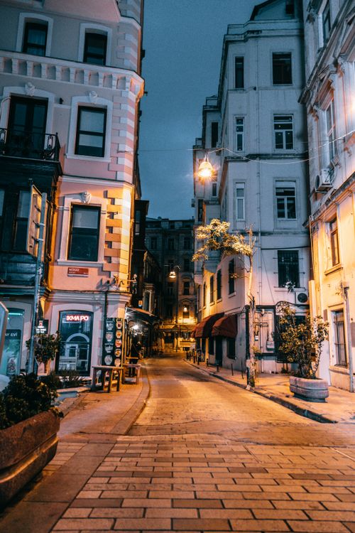 Free Empty cobblestone city street between aged residential houses with glowing lamps at night Stock Photo