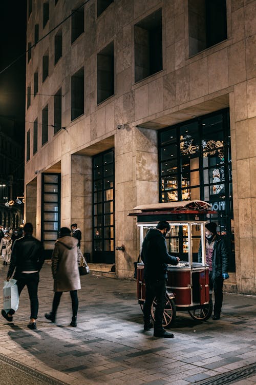 Free People strolling along busy street near building and hot dog cart at night Stock Photo