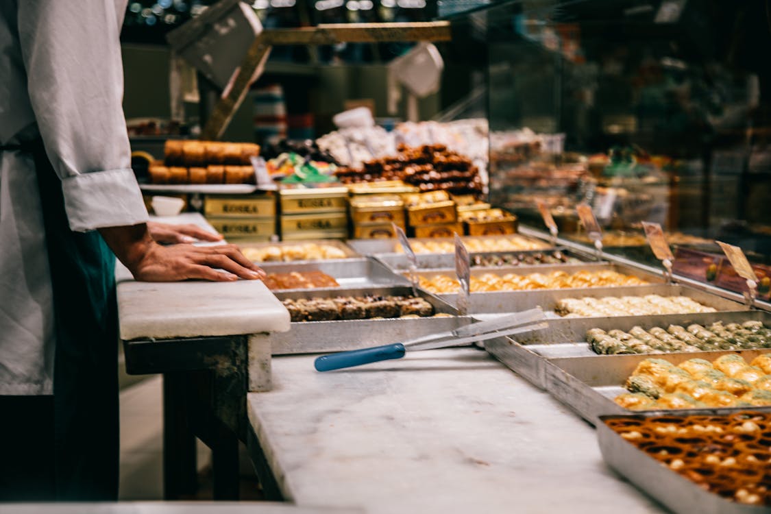 Crop anonymous male seller at counter with assorted traditional Turkish sweets in market