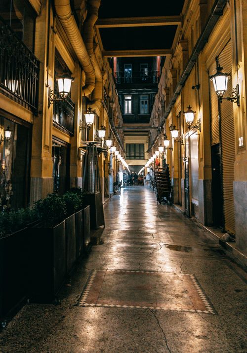 Free Empty pedestrian narrow street between old stone buildings illuminated with lamps at night Stock Photo
