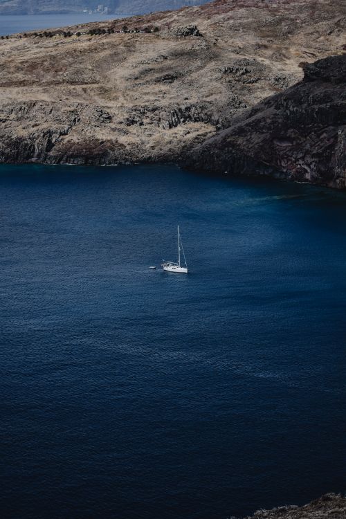 Free A lone sailboat navigates the deep blue waters near Madeira's rugged coastline, Portugal. Stock Photo