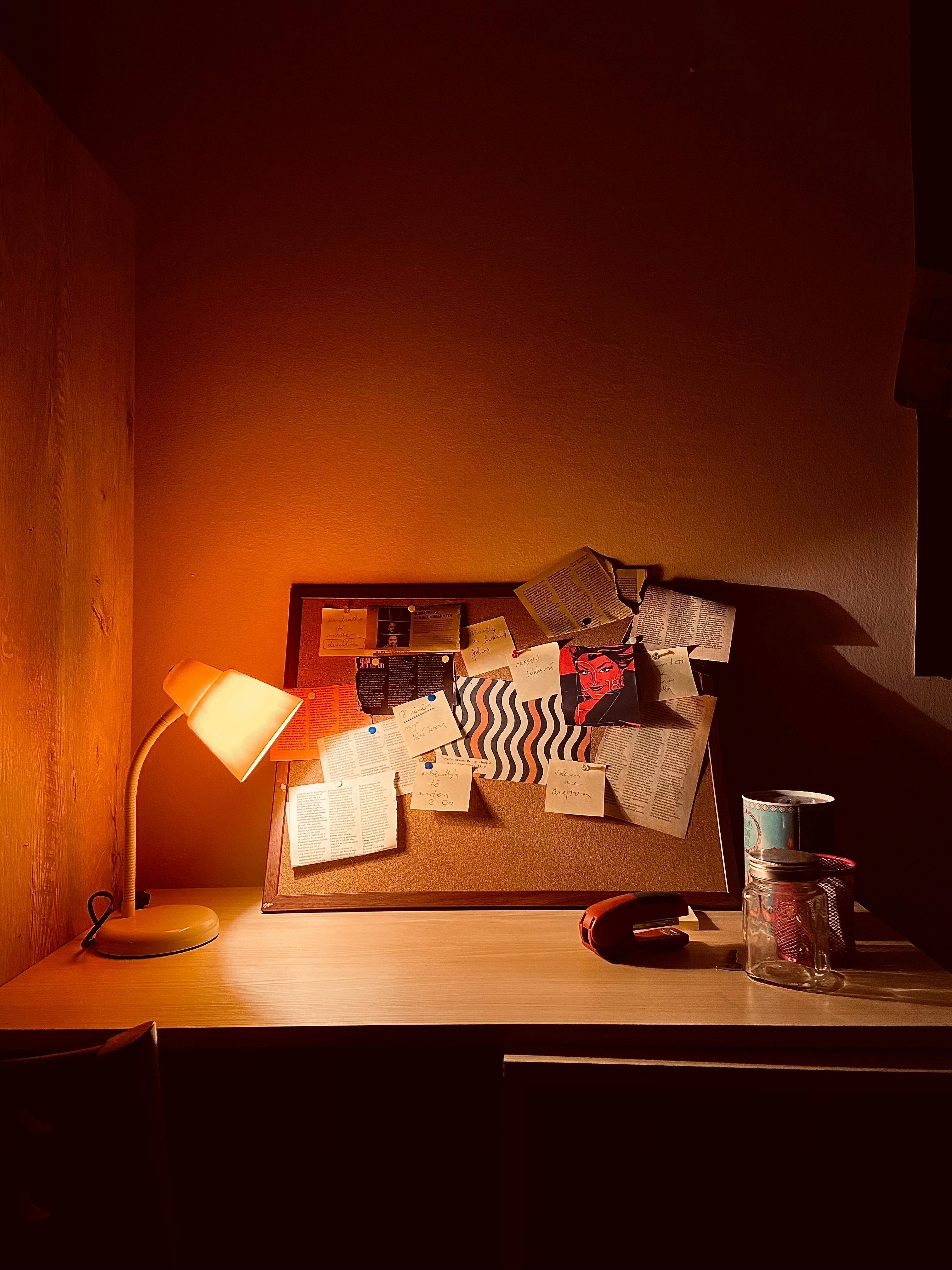 Free Warm, intimate workspace featuring a lamp-lit desk with a cluttered bulletin board. Stock Photo
