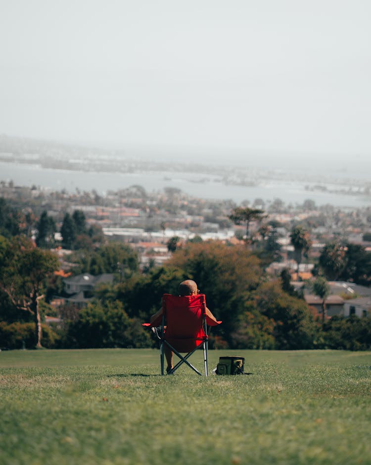 Person Sitting On Red Folding Chair On Green Grass Field